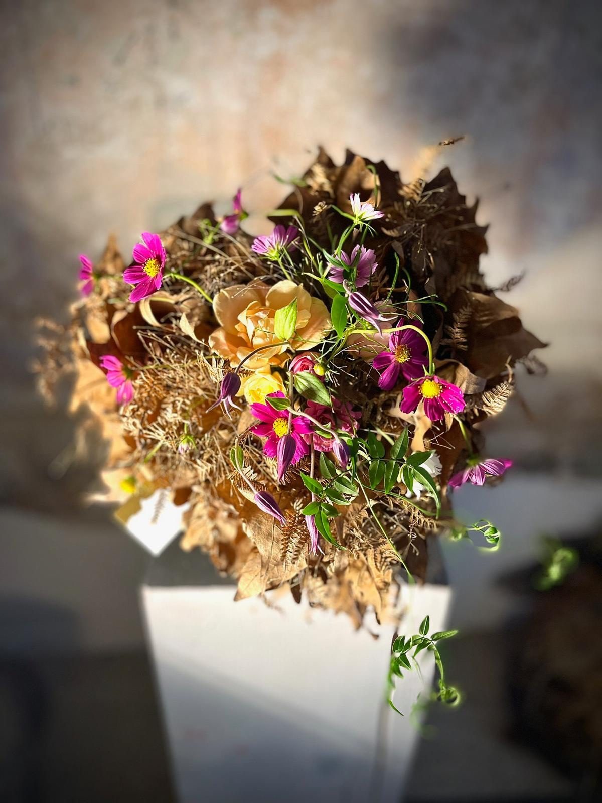 Bouquet autunnale di foglie secche e cosmos fucsia su plinto bianco